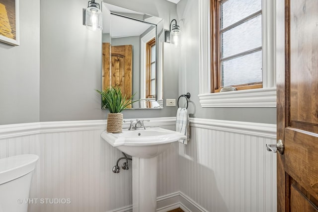 half bath featuring a sink, a wainscoted wall, and toilet