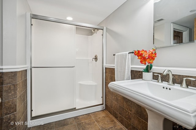 full bath featuring visible vents, tile walls, a stall shower, a sink, and a wainscoted wall