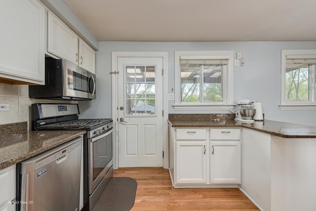 kitchen featuring appliances with stainless steel finishes, dark stone counters, white cabinetry, decorative backsplash, and light wood-type flooring