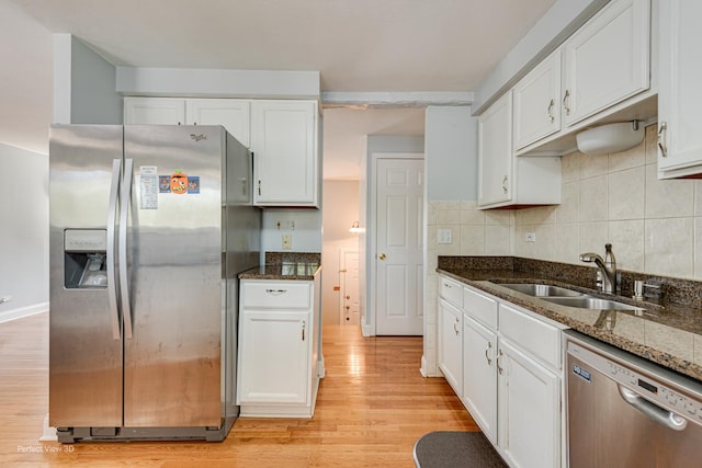 kitchen featuring appliances with stainless steel finishes, a sink, white cabinets, light wood-style floors, and dark stone counters