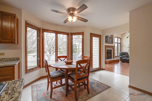 dining area with a tiled fireplace, light tile patterned floors, ceiling fan, and baseboards