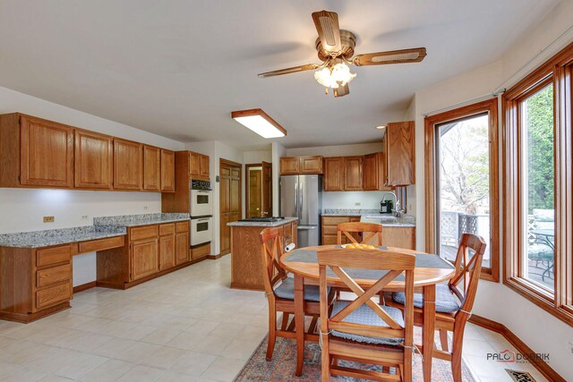 interior space with built in desk, a ceiling fan, brown cabinets, appliances with stainless steel finishes, and a sink