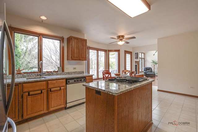 kitchen with a sink, ceiling fan, stainless steel appliances, a kitchen island, and stone countertops