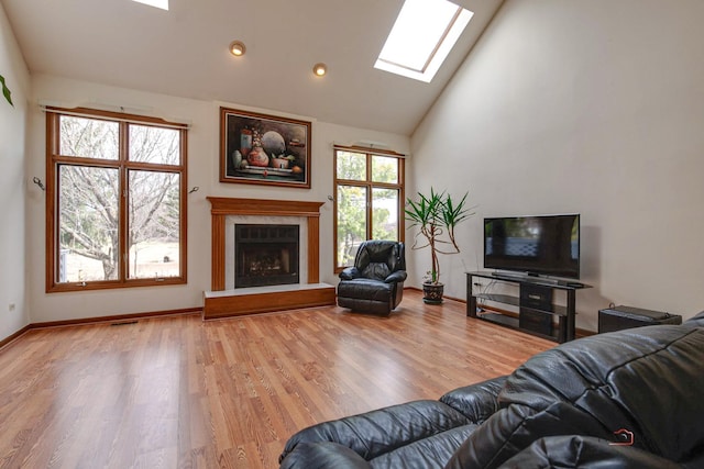 living area with high vaulted ceiling, a fireplace with raised hearth, a skylight, wood finished floors, and baseboards