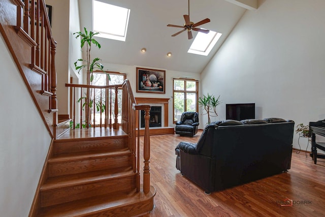 living area with a skylight, stairs, ceiling fan, high vaulted ceiling, and wood finished floors