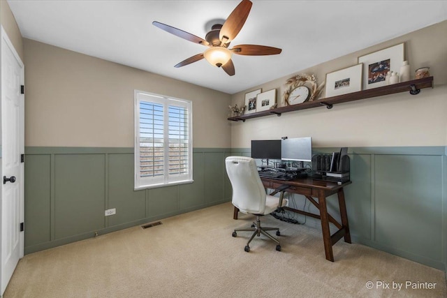 carpeted office space featuring a decorative wall, visible vents, a wainscoted wall, and ceiling fan