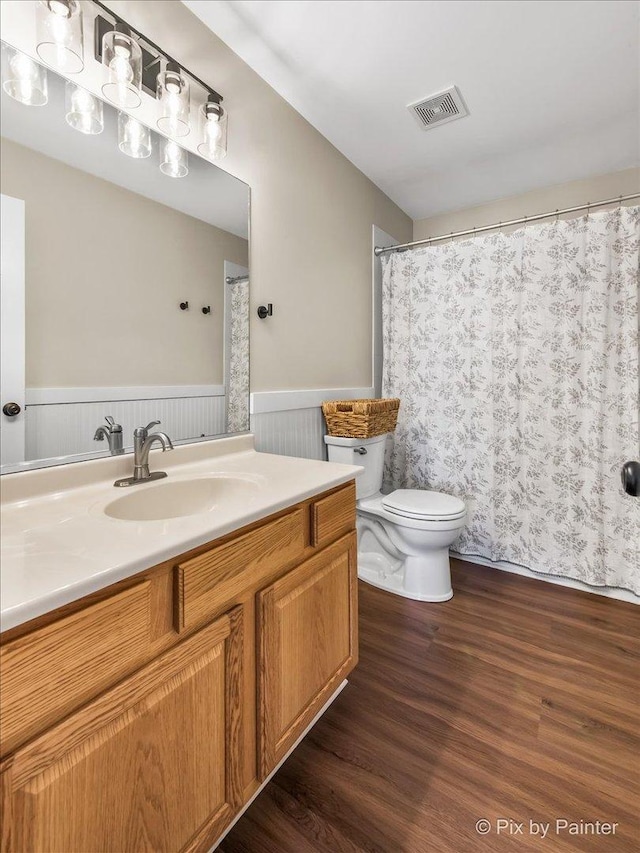 full bathroom with vanity, toilet, wainscoting, visible vents, and wood finished floors