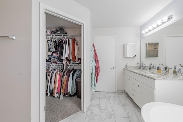 bathroom featuring a walk in closet, double vanity, marble finish floor, and a sink