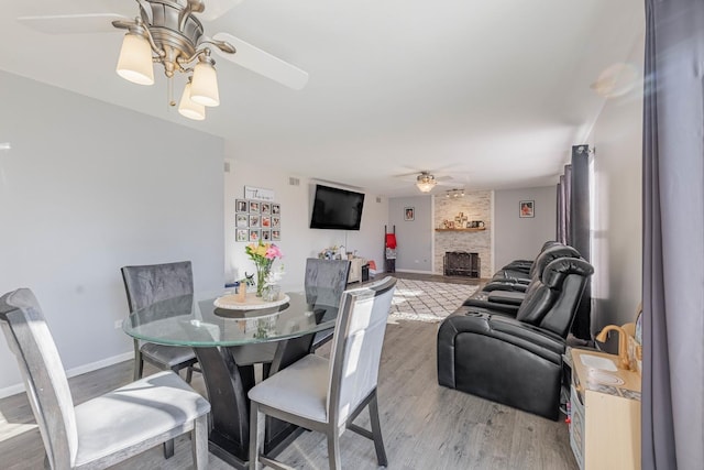 dining room featuring baseboards, a large fireplace, a ceiling fan, and wood finished floors
