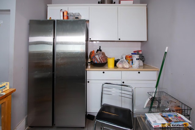 kitchen with white cabinetry, backsplash, light countertops, and freestanding refrigerator