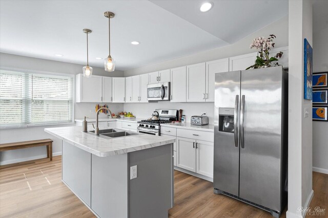 kitchen featuring white cabinets, a sink, stainless steel appliances, light wood-type flooring, and pendant lighting