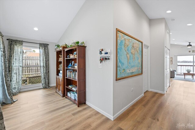 corridor with a healthy amount of sunlight, vaulted ceiling, recessed lighting, and light wood-style flooring