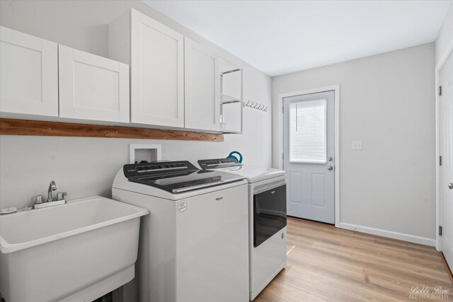 clothes washing area featuring independent washer and dryer, cabinet space, a sink, baseboards, and light wood-style flooring