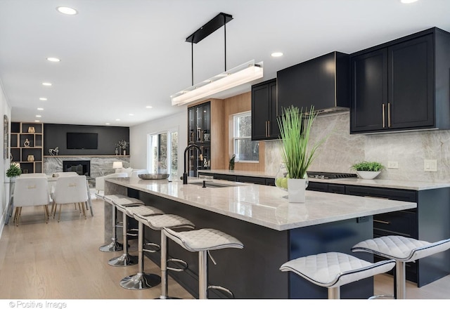 kitchen featuring dark cabinets, light stone countertops, tasteful backsplash, light wood finished floors, and a breakfast bar area