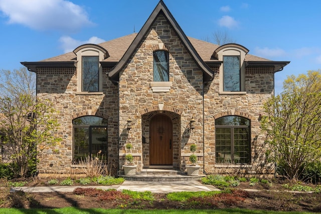 french country home featuring stone siding and a shingled roof