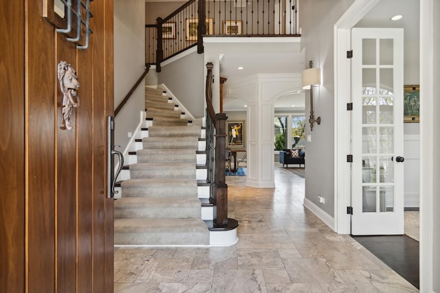 entryway with a towering ceiling, stone tile flooring, stairs, decorative columns, and arched walkways