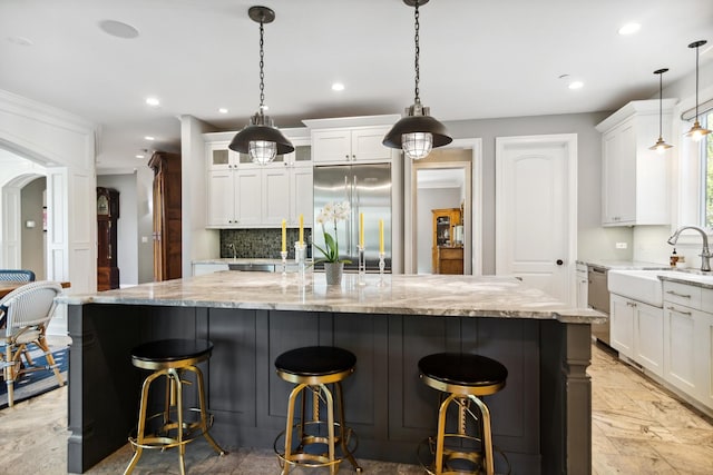 kitchen with a large island, a sink, built in fridge, white cabinetry, and backsplash
