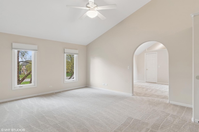 empty room featuring arched walkways, high vaulted ceiling, light colored carpet, and a ceiling fan
