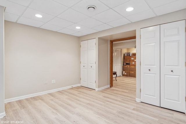 unfurnished bedroom featuring light wood-style floors, baseboards, two closets, and a drop ceiling