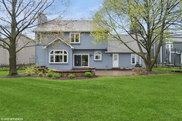 back of property with a lawn, a trampoline, roof with shingles, and fence