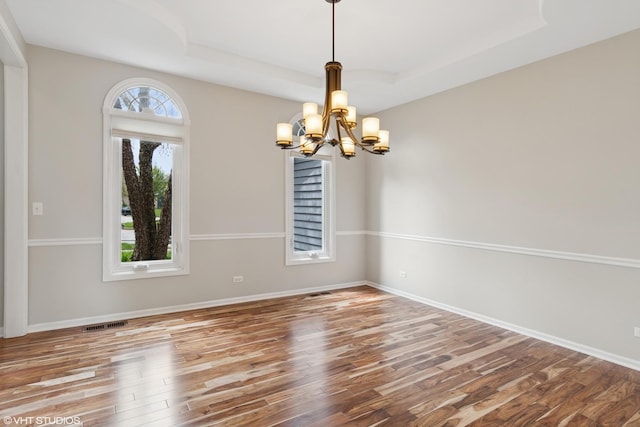 empty room featuring an inviting chandelier, a tray ceiling, wood finished floors, and visible vents