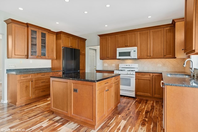 kitchen featuring wood finished floors, a kitchen island, white appliances, a sink, and dark stone countertops