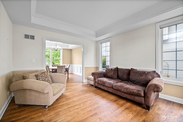 living area with a chandelier, light wood finished floors, a raised ceiling, crown molding, and wainscoting