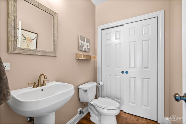 half bath featuring a sink, wood finished floors, toilet, and baseboards