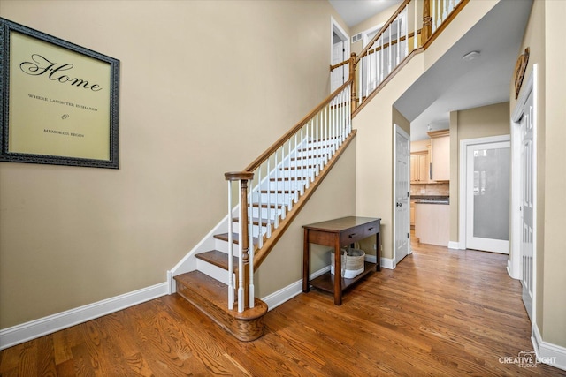 staircase featuring baseboards, wood finished floors, and a towering ceiling