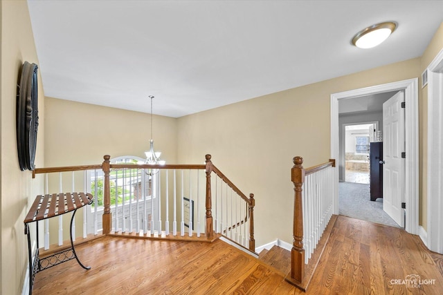 corridor featuring an upstairs landing, a chandelier, wood finished floors, and baseboards