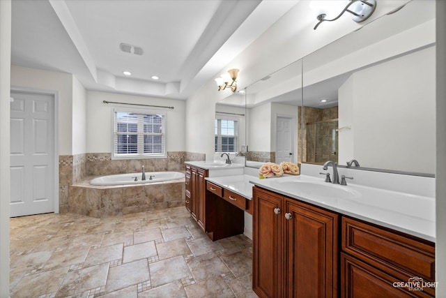 bathroom with a shower stall, a garden tub, two vanities, a raised ceiling, and stone finish flooring