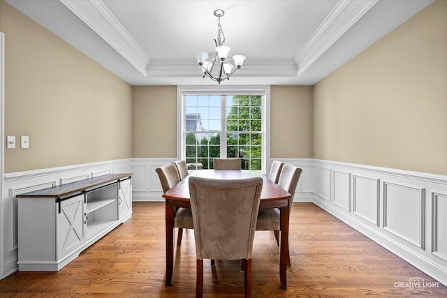 dining space featuring a chandelier, crown molding, light wood-type flooring, a raised ceiling, and wainscoting