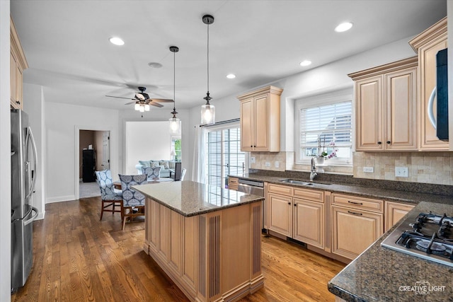 kitchen with a sink, stainless steel appliances, a ceiling fan, tasteful backsplash, and a center island