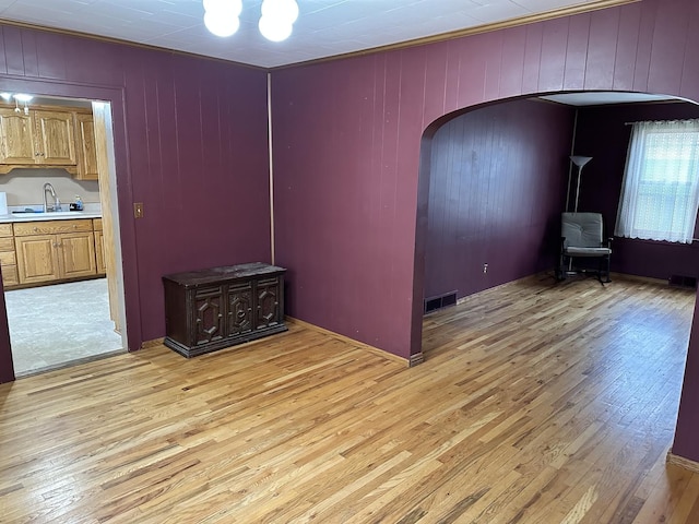 empty room featuring light wood-style flooring, arched walkways, a sink, and visible vents