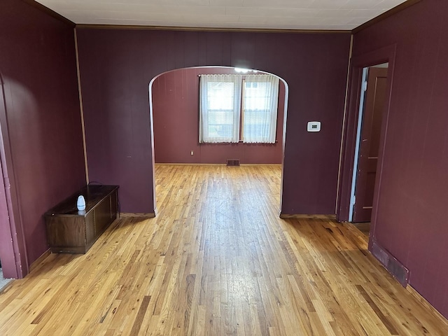 empty room with arched walkways, ornamental molding, visible vents, and light wood-type flooring