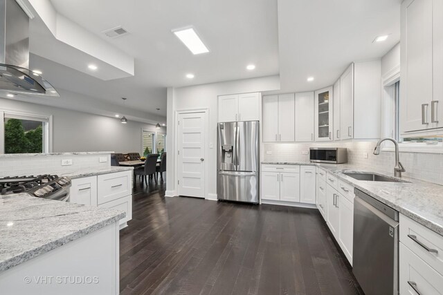 kitchen featuring wall chimney range hood, backsplash, appliances with stainless steel finishes, a sink, and light stone counters