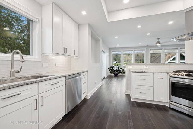 kitchen featuring dark wood-style flooring, appliances with stainless steel finishes, a sink, white cabinetry, and tasteful backsplash