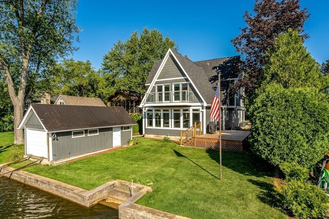 rear view of property featuring roof with shingles, a deck with water view, a garage, a lawn, and an outdoor structure