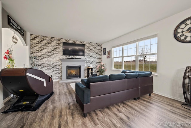 living room with a warm lit fireplace, baseboards, and wood finished floors