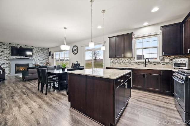 kitchen with tasteful backsplash, a sink, open floor plan, light wood-style floors, and range with gas stovetop