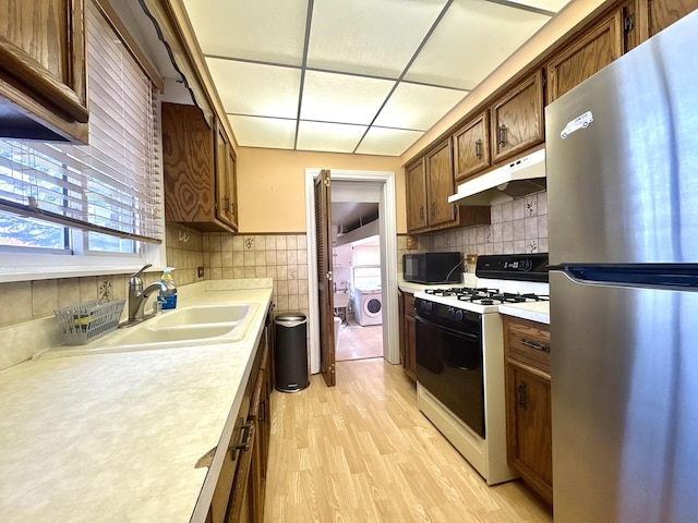 kitchen with a sink, freestanding refrigerator, gas stove, black microwave, and under cabinet range hood