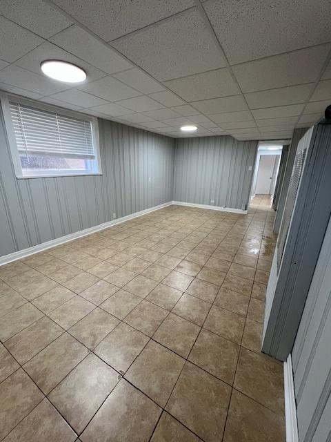 finished below grade area with light tile patterned flooring, baseboards, and a drop ceiling