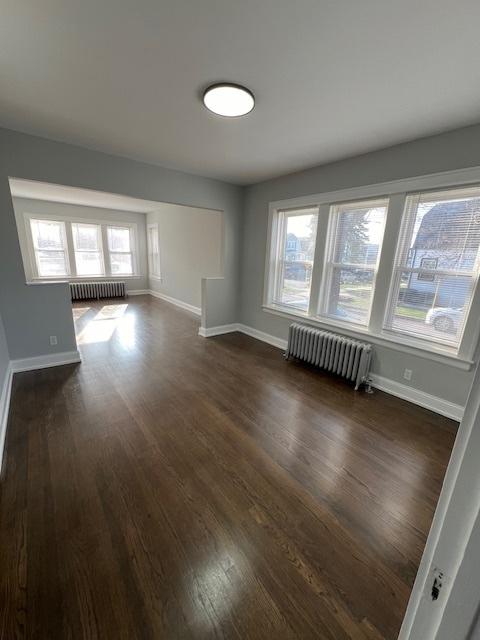 spare room with baseboards, radiator, and dark wood finished floors