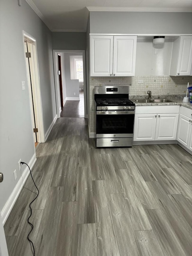 kitchen with tasteful backsplash, stainless steel range with gas stovetop, a sink, white cabinetry, and wood finished floors