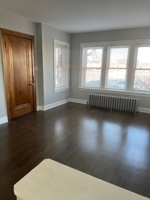 spare room featuring radiator heating unit, baseboards, and dark wood finished floors