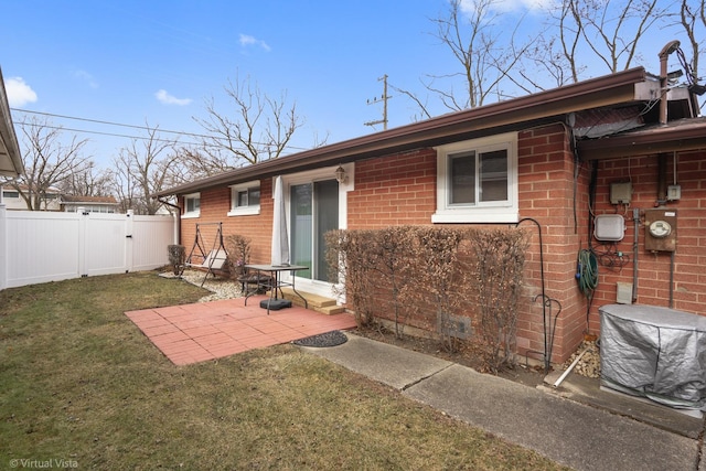 rear view of property with brick siding, fence, a patio, and a lawn