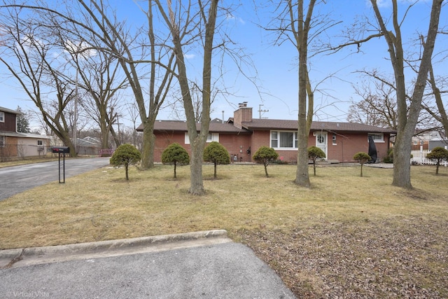 ranch-style home with brick siding, a front lawn, aphalt driveway, and a chimney