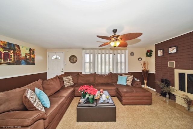 carpeted living area featuring a fireplace, a ceiling fan, and a wainscoted wall