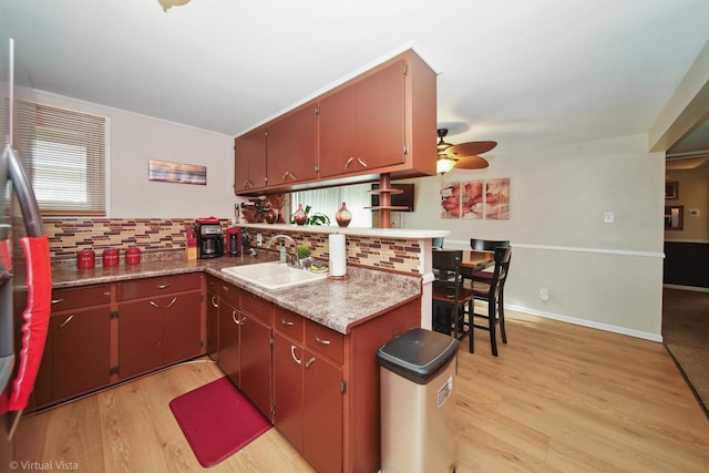 kitchen featuring a peninsula, a ceiling fan, backsplash, light wood-style floors, and a sink