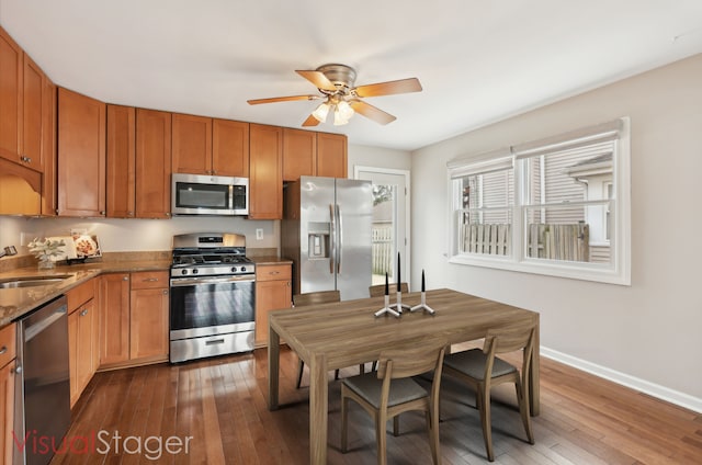 kitchen with a ceiling fan, dark wood-style flooring, a sink, stainless steel appliances, and baseboards